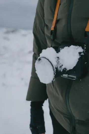 Un appareil photo couvert de neige, suspendu à sa sangle sur une veste kaki.