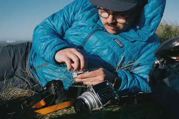 Jeremy, allongé dans l'herbe, chargeant un nouveau roulant dans son Hasselblad