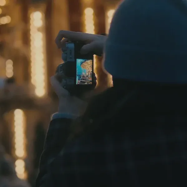 Une personne de dos photographie un manège illuminé la nuit, l’écran de l’appareil affichant l’image cadrée.