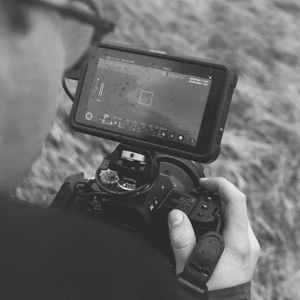 Un moniteur externe fixé sur un appareil photo affiche un cadre de visée, dunes herbeuses en arrière-plan, noir et blanc.