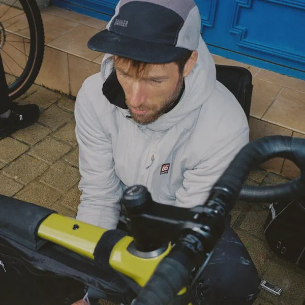 Un homme casquette règle un sac de guidon sur un vélo jaune, devant une porte bleue.