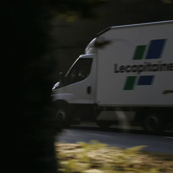 Un camion frigorifique blanc roule sur une route bordée d’arbres, vu en flou de mouvement depuis un fourré.