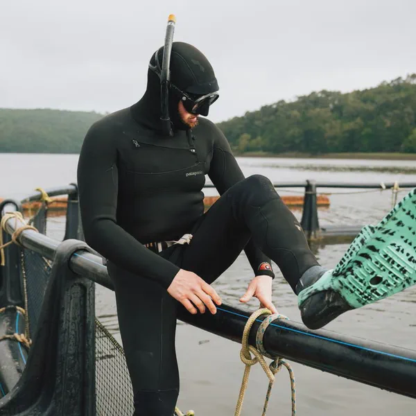 Yves Quéré assis sur la rambarde d’un parc à moules, masque et tuba sur la tête, combinaison de plongée noire.