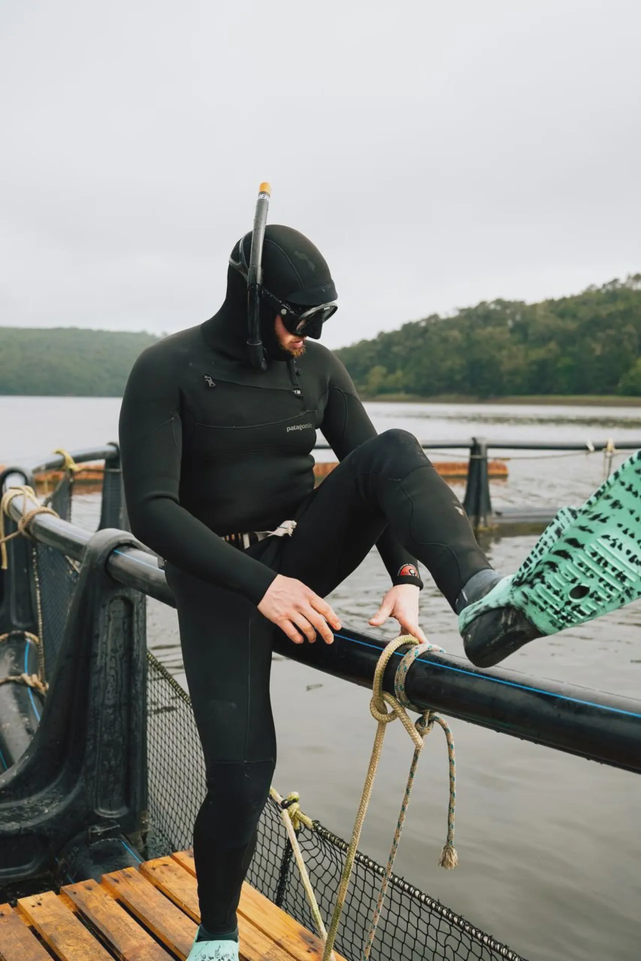 Yves Quéré assis sur la rambarde d’un parc à moules, masque et tuba sur la tête, combinaison de plongée noire.