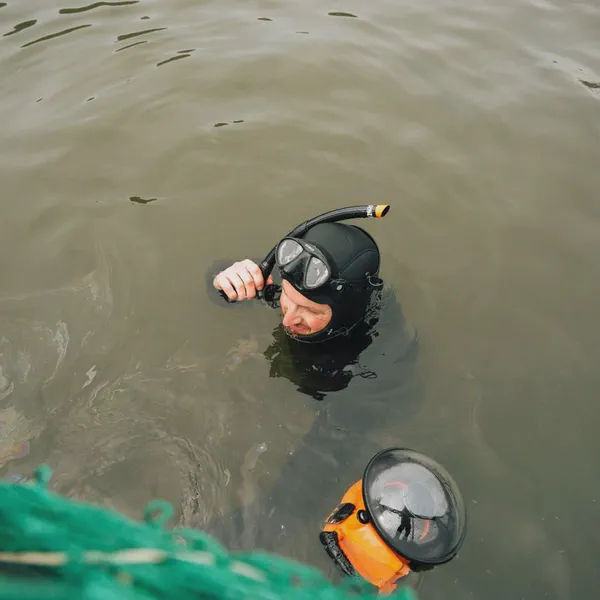 Yves Quéré émerge de l’eau trouble, masque et tuba sur la tête, boîtier de caméra orange flottant à côté de lui.