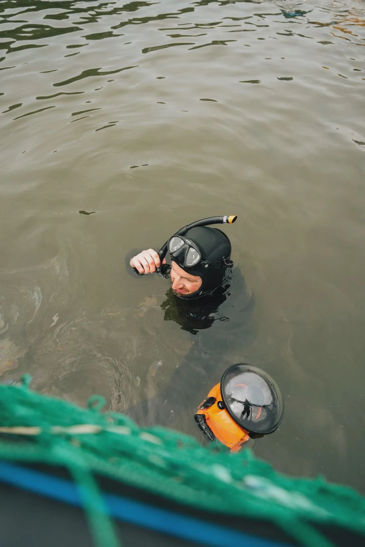 Yves Quéré émerge de l’eau trouble, masque et tuba sur la tête, boîtier de caméra orange flottant à côté de lui.