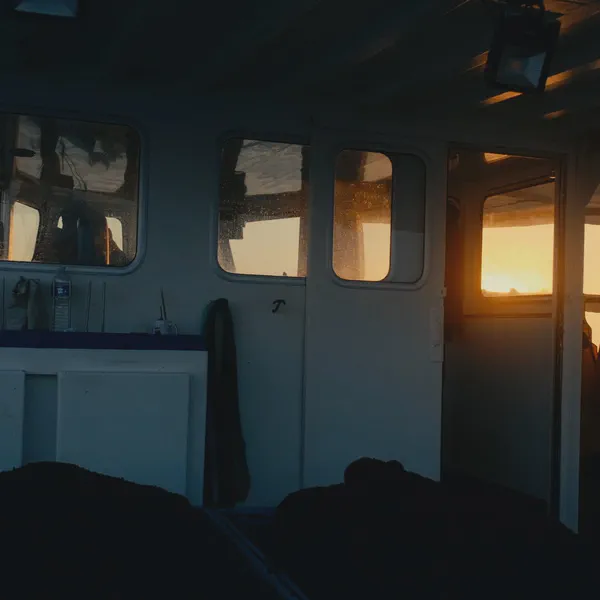 Intérieur d’une cabine de bateau au coucher du soleil, cirés suspendus, porte ouverte sur la lumière du soir.