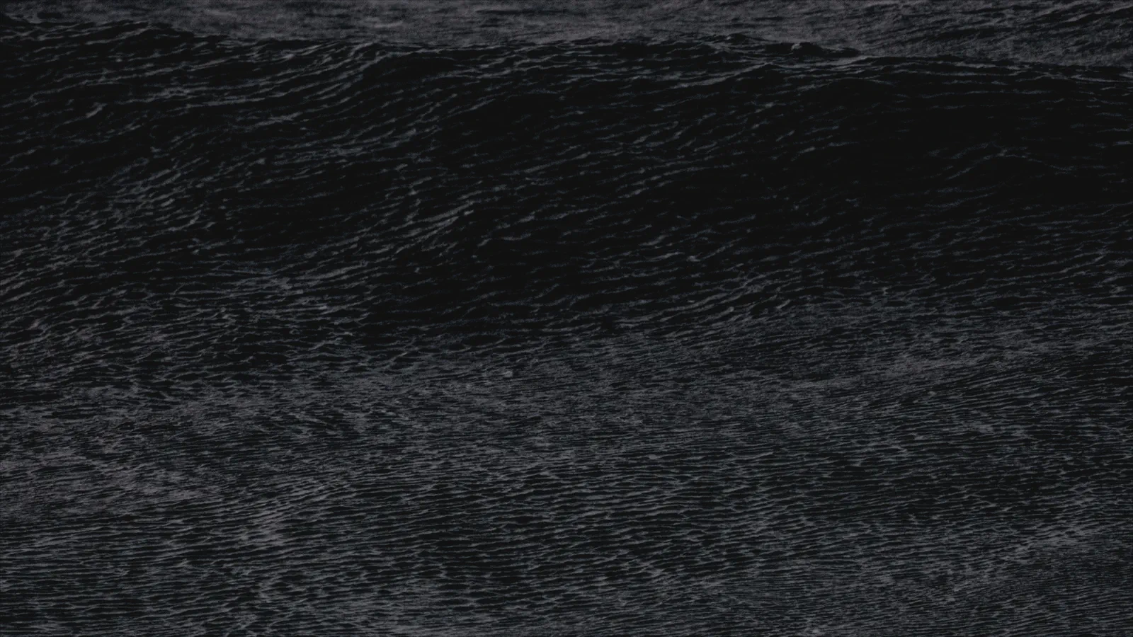 Gros plan sur une crête de vague sombre et texturée, mousse blanche visible par endroits, sans horizon.