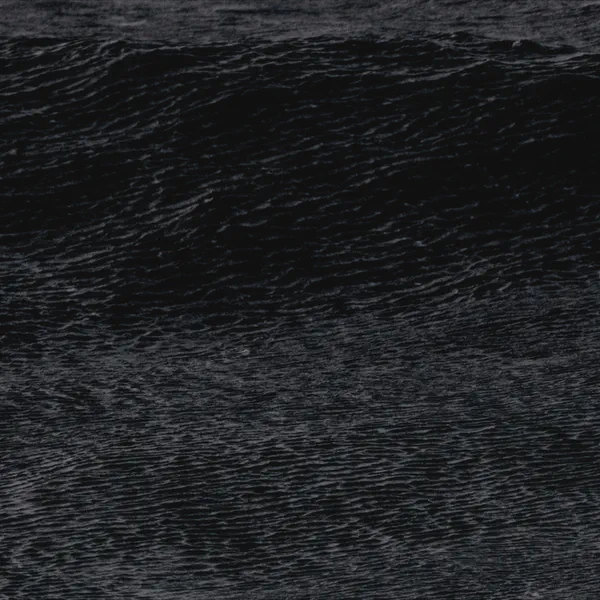 Gros plan sur une crête de vague sombre et texturée, mousse blanche visible par endroits, sans horizon.