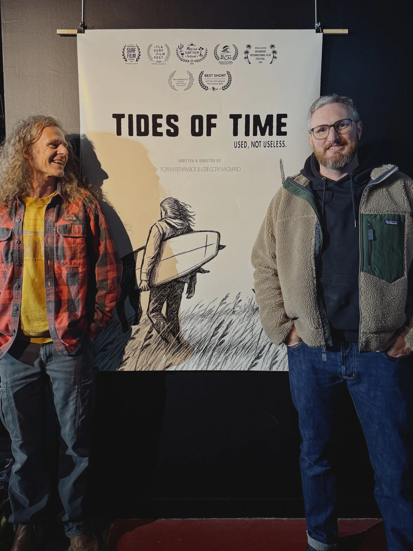 Yoann Renambot et Grégory Mignard posants devant l'affiche du film Tides of Time pendant le Brest Surf Film Festival