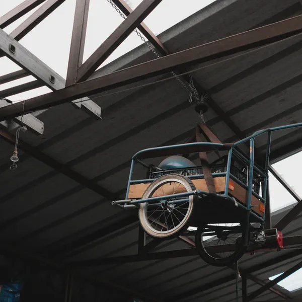 Une remorque à vélo contenant un casque est suspendue à la charpente d’un atelier.
