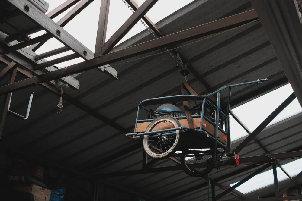 Une remorque à vélo contenant un casque est suspendue à la charpente d’un atelier.
