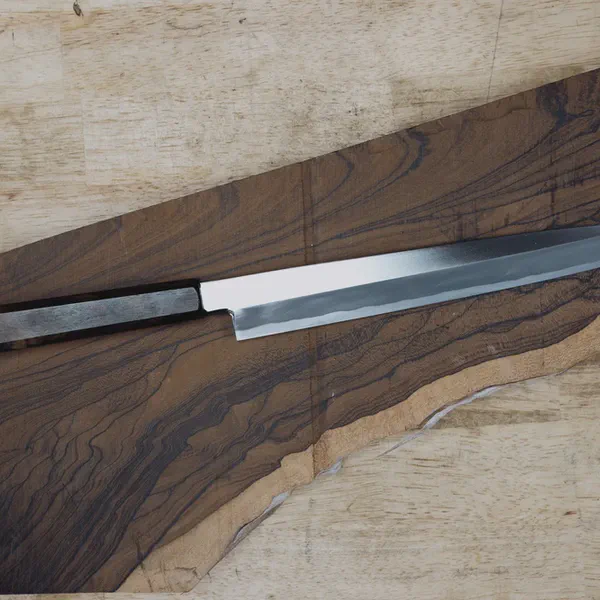 Un couteau fini au manche sombre repose en diagonale sur une planche de bois aux veines marquées.