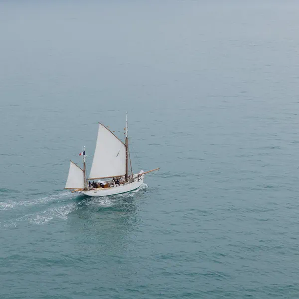 Un voilier traditionnel toutes voiles dehors navigue sur une mer calme, sillage blanc derrière la coque.
