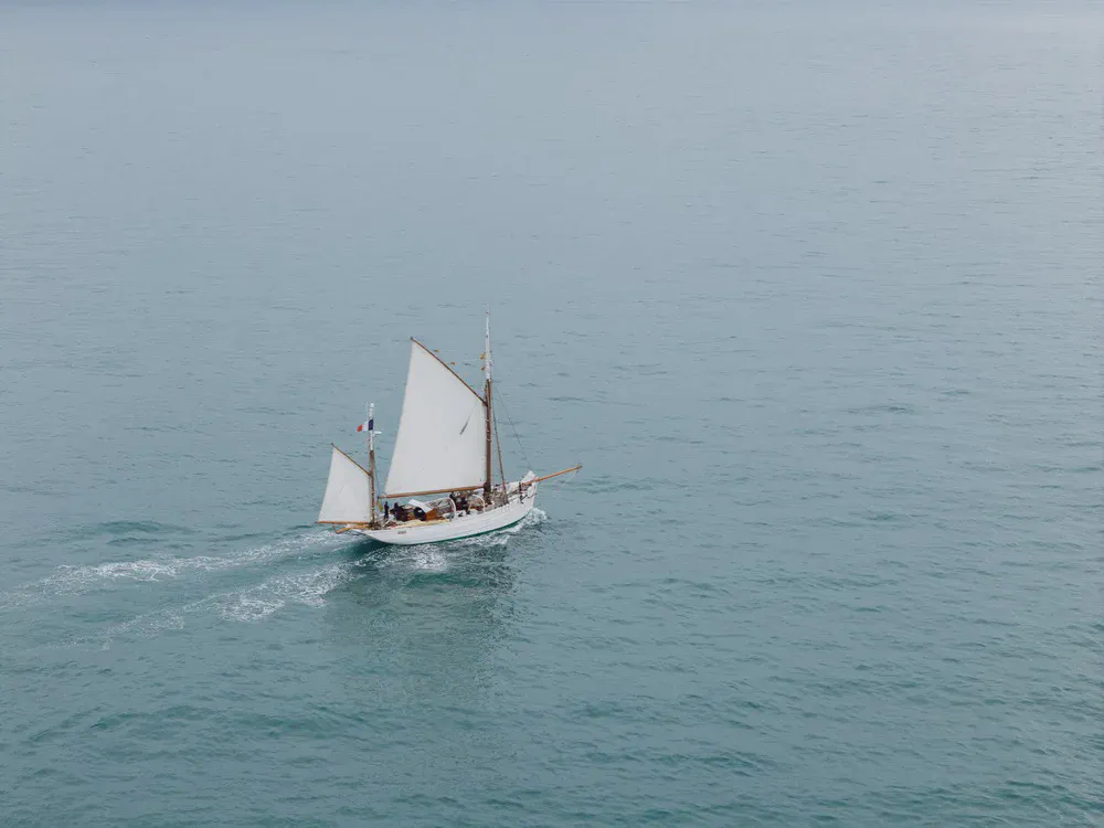 Un voilier traditionnel toutes voiles dehors navigue sur une mer calme, sillage blanc derrière la coque.